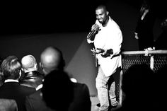 a black and white photo of a man holding a microphone in front of an audience