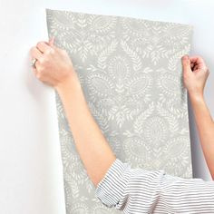 a woman is holding up a piece of fabric on the wall with her hands and arm