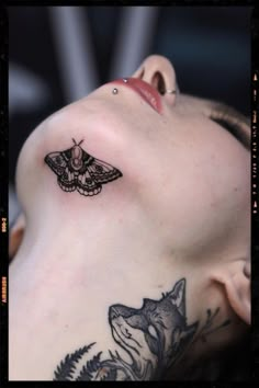 a woman with a moth tattoo on her shoulder and neck, laying down next to a wolf