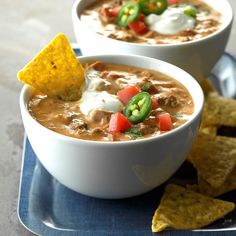 two bowls of chili and cheese soup with tortilla chips on the side, ready to be eaten