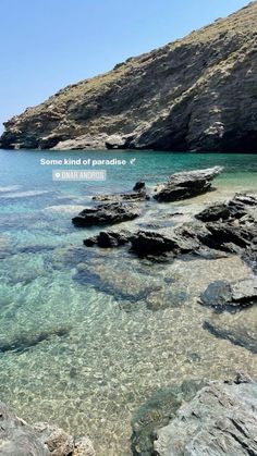 the water is crystal clear and there are rocks on the shore near the beach with an island in the background