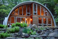 an unusual house in the woods with lots of windows and plants on the rocks outside