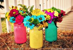 three mason jars filled with colorful flowers sitting on hay next to a white picket fence