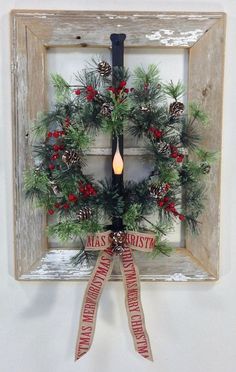 a christmas wreath hanging on a wall with a candle and ribbon in front of it