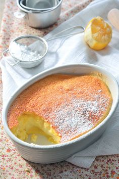 a cake in a white dish with powdered sugar on top and two lemons next to it