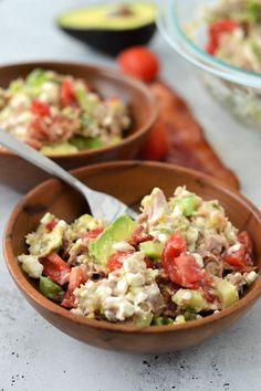 two wooden bowls filled with salad sitting on top of a white counter next to tomatoes and cucumbers