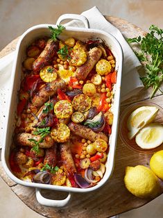 a casserole dish with meat, vegetables and lemons on a wooden table