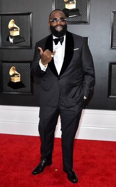 a man in a tuxedo poses on the red carpet at an awards event