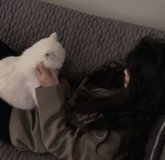 a woman laying on top of a couch holding a white cat