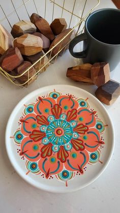 a white plate with an orange and blue flower design on it next to a cup of coffee