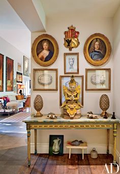 a room with pictures on the wall and paintings on the wall above it, along with an ornate console table