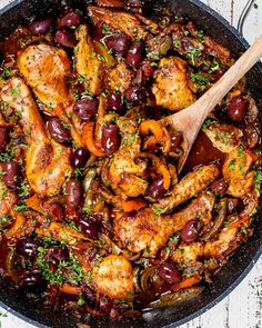 chicken and olives in a skillet with a wooden spoon