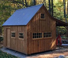 a small wooden building with a metal roof in the middle of some trees and rocks