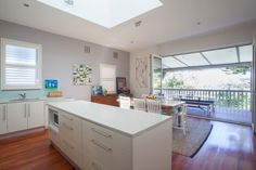 an open kitchen and dining room with skylights in the ceiling, hardwood flooring, and white cabinetry