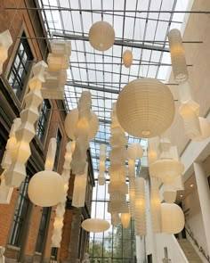 several white paper lanterns hanging from the ceiling in a building with glass windows and skylights