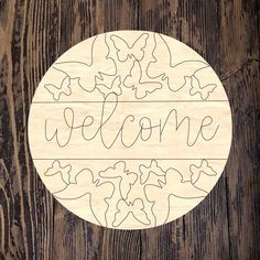 a wooden sign that says welcome with butterflies in the center on a wood table top