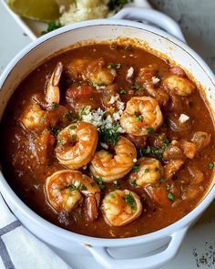 a white bowl filled with shrimp and tomato soup on top of a table next to bread