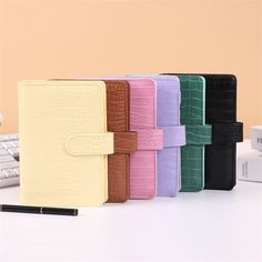 four different colored notebooks sitting on top of a desk next to a computer keyboard