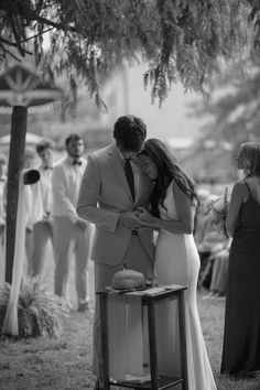 black and white photo of bride and groom cutting their wedding cake at outdoor ceremony with guests in the background