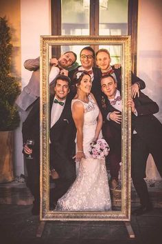 a group of people that are standing in front of a photo frame with a bride and groom