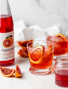 a bottle of thatche blood orange punch next to two glasses filled with it