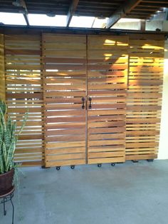 a large wooden gate next to a potted plant in front of a wall with slats on it