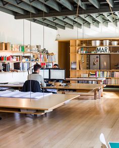 two people sitting at desks in an open room with bookshelves and shelves