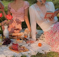 two women sitting on a blanket with food and drinks in front of them while reading books