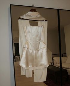 a white dress hanging on a hanger in front of a mirror with a couch behind it