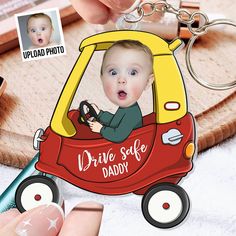 a hand holding a keychain with a photo of a baby in a car