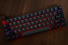 a black and red keyboard on a wooden table with wires attached to it's sides