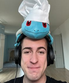 a man wearing headphones and a hat with a pokemon character on top of his head