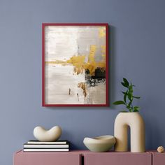 an abstract painting hangs on the wall above a pink cabinet with two white vases