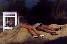 a woman laying on top of a pile of sand next to a phone booth and trees