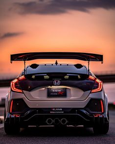 the back end of a white car with its hood open at sunset in front of a body of water