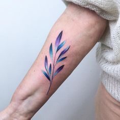 a woman's arm with blue and purple leaves on it