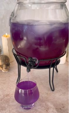 a purple liquid is being poured into a large glass bowl with a metal stand on the floor