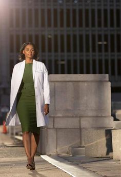 a woman in a green dress and white coat walking down the street