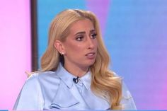 a woman with long blonde hair sitting in front of a tv screen wearing a blue shirt and earrings