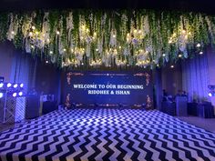 a stage set up for a wedding reception with chandeliers and flowers hanging from the ceiling