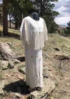 a white dress with fringes on it sitting in the grass next to some trees