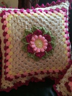 a crocheted pillow with a pink flower on the front and green leaves on the back