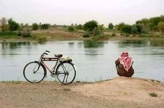 a bike parked next to a river with a blanket on it's back and a person sitting by the water