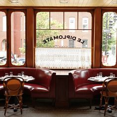 two booths with tables and chairs in front of large windows that look out onto the street