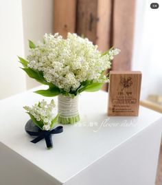 a bouquet of white flowers sitting on top of a table next to a wooden block