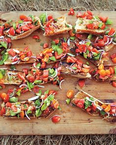 a wooden cutting board topped with slices of toasted bread covered in veggies