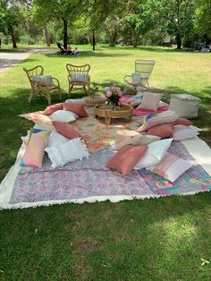 an outdoor picnic with lots of pillows on the ground and chairs in the grass around it