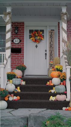 front porch decorated for fall with pumpkins, gourds and flowers on the steps