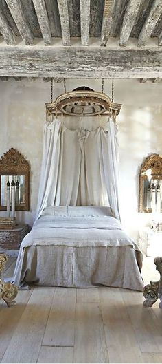 an old fashioned bedroom with white bedding and antique mirrors on the wall above it