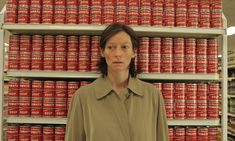 a woman standing in front of stacks of red and white cans, with her hands on her hips